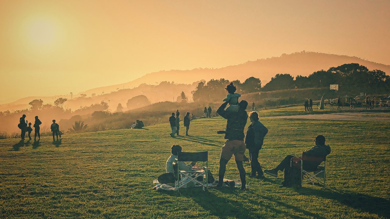 A golden-hour hilltop with people gathered in the haze