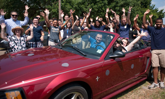 A crowd throwing their arms up behind a red convertible at a Love Drop for the Stalnaker family