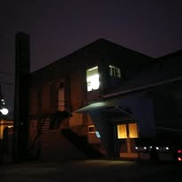 The building from the parking lot at dusk, a window lit